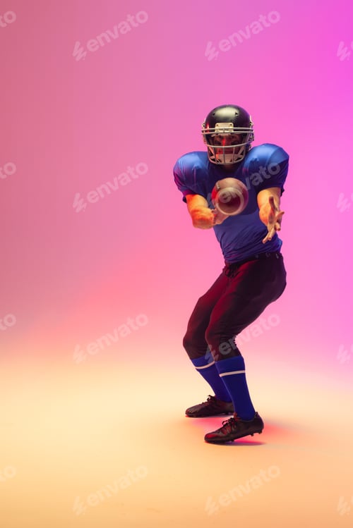Preview: Caucasian male american football player holding ball with neon pink lighting
