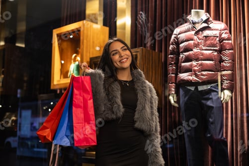Preview: Low-angle shot of smiling young latina shopping through city stores at night