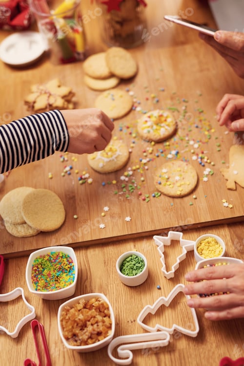 Preview: Close up of woman’s hands decorating cookies for Christmas