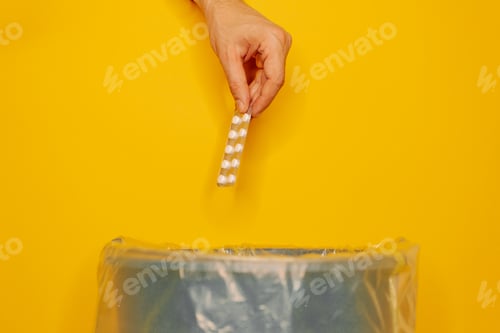 Preview: Closeup shot of a man putting a pack of pills in a trash can on a yellow background