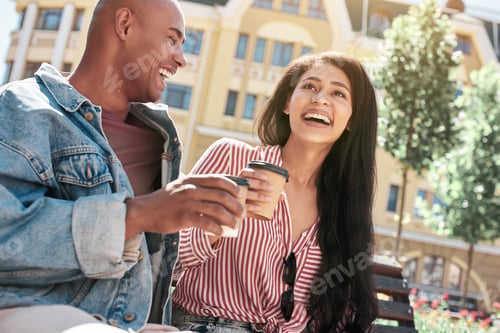 Preview: Romantic Relationship. Young diverse couple sitting on bench on the city street holding cups