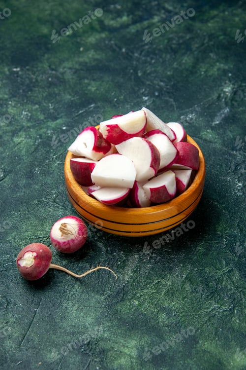 Preview: Above view of whole and chopped fresh radishes inside and outside of a wooden bowl on dark color