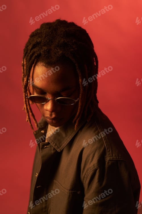 Preview: Young Black Man Wearing Sunglasses Looking down Against Red Studio Background