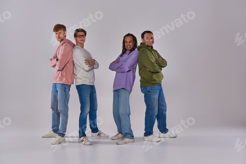Preview: four young men standing back to back and smiling at camera on grey backdrop, cultural diversity