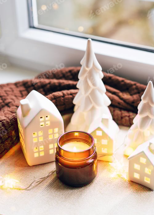 Visualização: Cena de Natal aconchegante com casas de cerâmica e luz de velas perto de uma janela