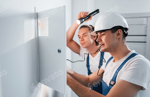 Preview: Two young male electricians works indoors together. Using flashlight