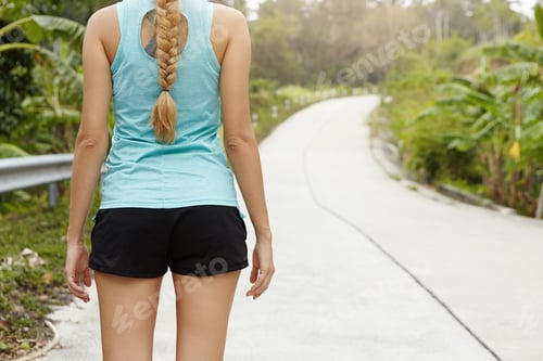 Preview: Back view of blonde woman runner with beautiful body dressed in sportswear standing on road in tropi
