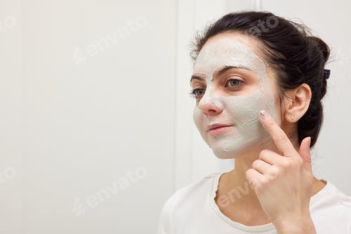Preview: Caucasian woman looking in mirror and applying face mask