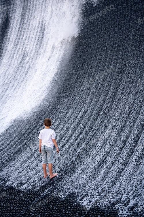 Preview: A boy in denim shorts and a white T-shirt looks at an artificial waterfall.