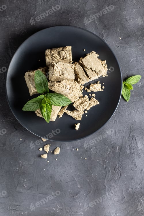 Preview: Pieces of halva on black plate. Sweet dessert with mint leaves on black background