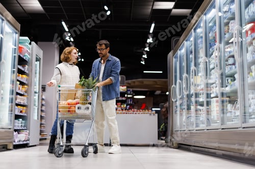 Preview: Couple discussing shopping list while pushing cart in supermarket