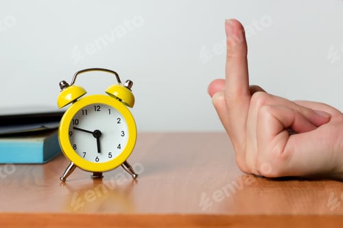 Preview: Female hand showing the middle finger to the alarm clock in the early morning