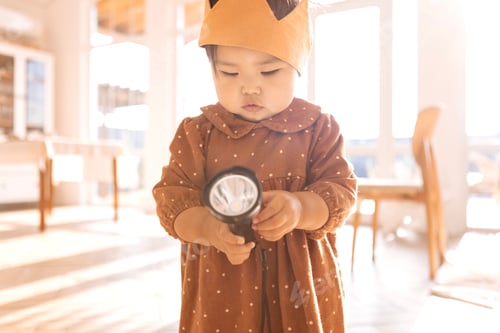Preview: Cute Asian babe is playing with a flashlight at home. A little Korean girl in a dress