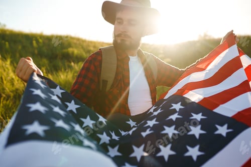 Preview: 4th of July. American Flag. Traveler with flag of America. Man in hat, backpack, a shirt and jeans.