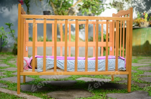 Preview: Baby crib with soft mattress and a cozy sheets, stylish wooden finish on the crib side view.