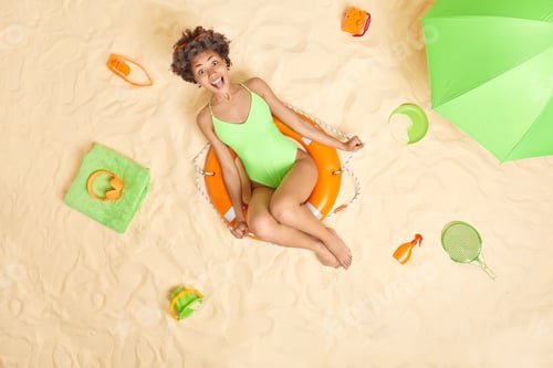 Preview: Joyful young Afro American woman with happy expression poses on lifebuoy wears green bikini has fun