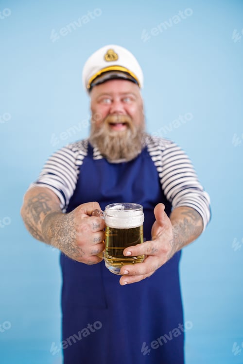 Preview: Smiling obese man sailor stands on light blue background, focus on hands with beer