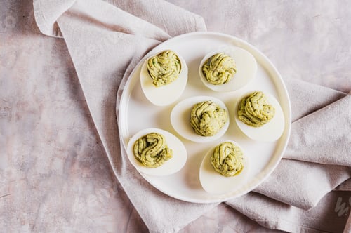 Preview: Close up of eggs stuffed with avocado and yolk mixture on a plate on a table top view