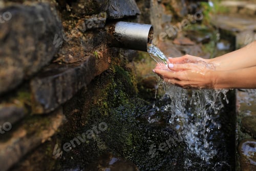 Preview: Woman collect pure water in hand palm from the source in the wall, hold and drink it.