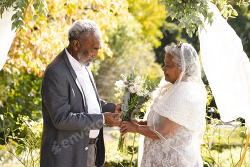 Preview: Happy senior biracial bride and groom during wedding ceremony in sunny garden