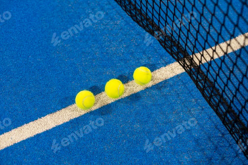 Preview: several balls by the net on a blue paddle tennis court