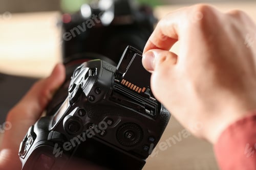 Preview: Man inserting SD memory card into photo camera indoors, closeup