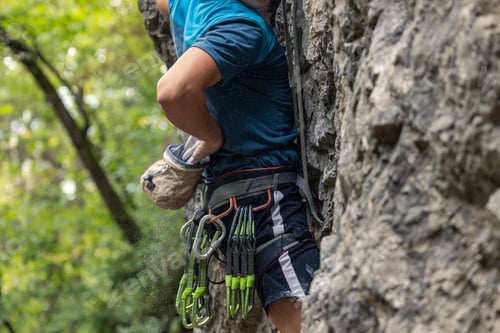 Preview: Shallow focus of a young climber climbing up a rocky mountain with ropes in the countryside