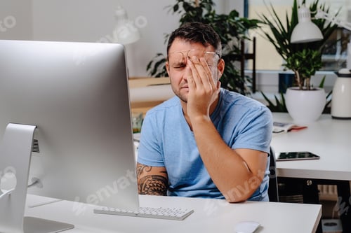 Preview: Tired male office worker at table on his workplace with desktop computer
