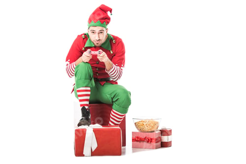 Preview: man in christmas elf costume sitting on pile of presents and playing video game isolated on white