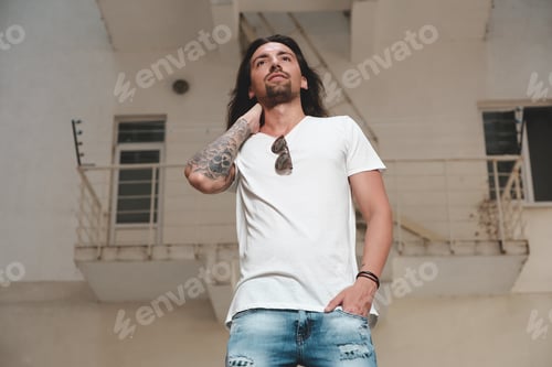 Vista previa: Elegante hombre barbudo con pelo largo y tatuajes posando