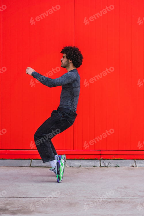 Preview: Vertical shot of a Caucasian young athlete posing in front of a red wall