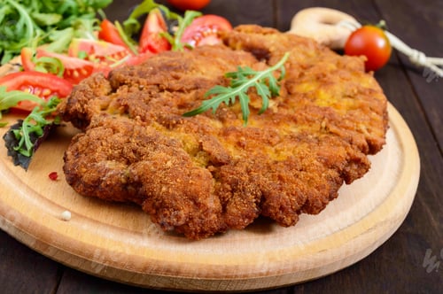 Preview: A large Viennese schnitzel and tomato salad on a cutting board