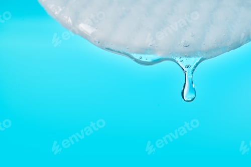 Preview: Cotton pad absorbing cosmetic serum drop on blue background