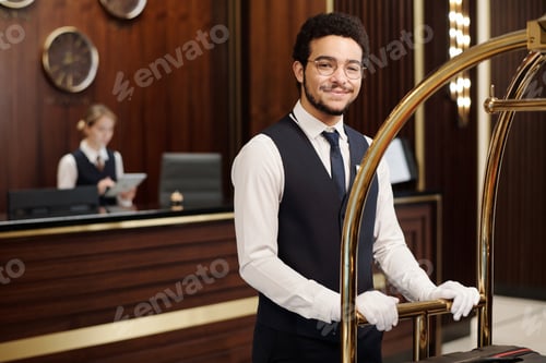 Preview: Young elegant bellboy pushing cart with clients baggage