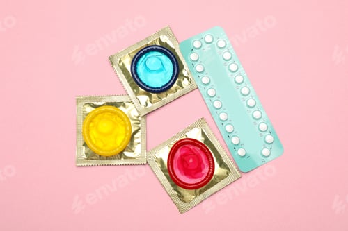 Preview: Condoms and birth control pills on pink background, top view. Safe sex