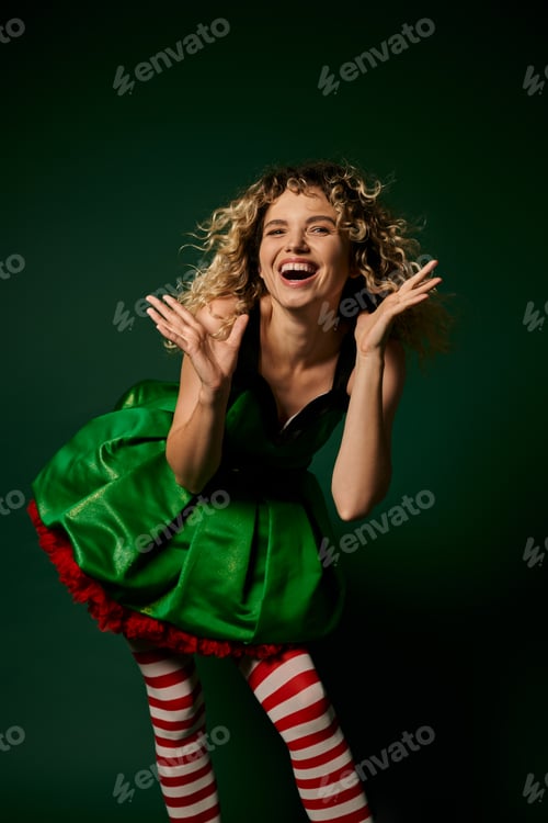 Preview: cheerful curly woman dressed as new year elf smiling happily at camera with hands raised face