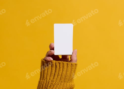 Preview: Female hand holding empty paper white business card on a yellow background. Copy space