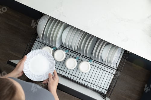Preview: Woman Arranging Clean Dishes in Modern Kitchen During Morning Hours