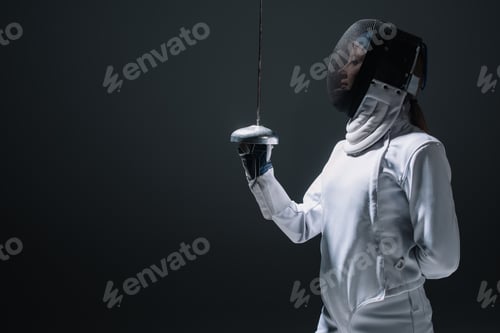 Preview: Side view of fencer in fencing mask holding rapier isolated on black