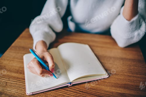 Preview: Female with pink manicure writing by blue pen in notebook