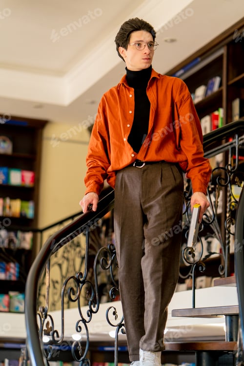 Preview: a young guy in glasses goes down the stairs with a book in his hands in library