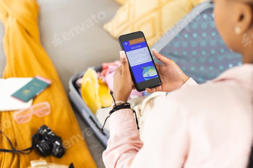 Preview: A young African American woman checks her phone, surrounded by travel essentials