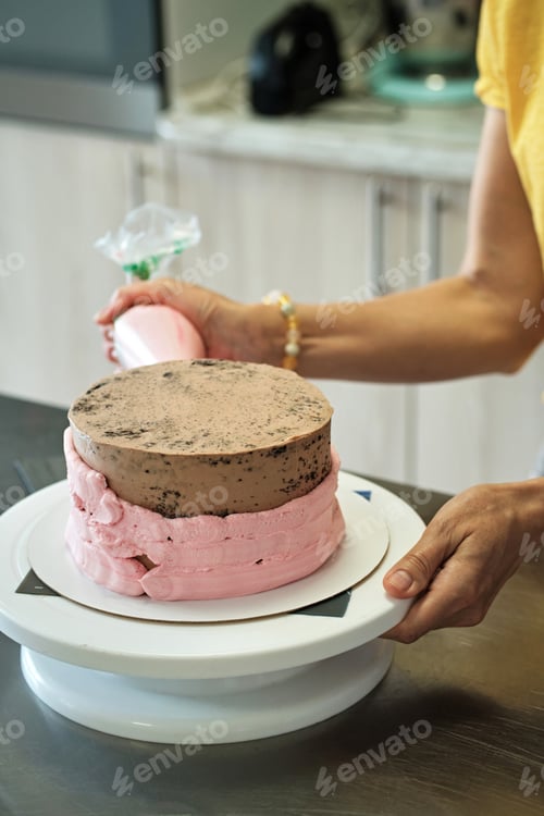 Vorschau: Frau macht Schokoladenkuchen mit rosa Sahne, Nahaufnahme. Prozess der Kuchenherstellung, Selektiver Fokus