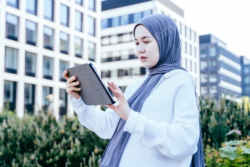 Preview: Focused Muslim woman using tablet in eco-urban setting