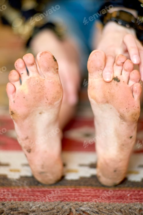 Preview: Bare, dirty feet with visible toes of a person resting on a colorful, patterned rug.