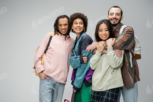 Preview: cheerful and trendy multicultural friends with backpacks posing isolated on grey