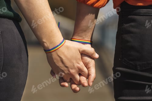 Preview: intertwined hands of lesbian couple with a rainbow bracelet