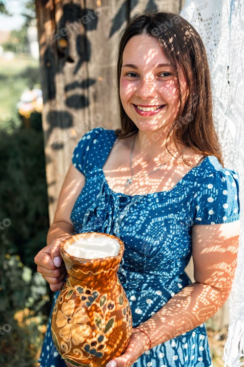 Preview: Young farmer woman smiling on camera carries jug of milk after milking cow on farm pasture. Natural