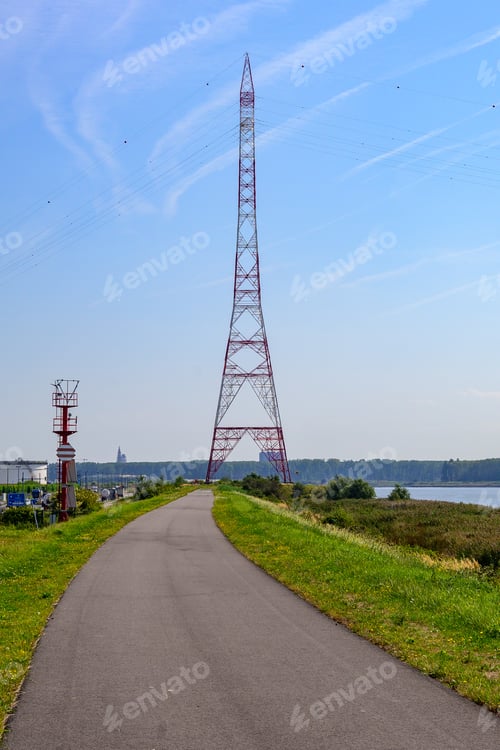 Preview: Asphalted road to a red electricity pylon next to the water in Port of Antwerp, Belgium.