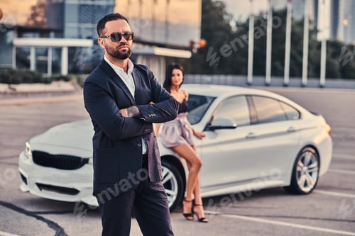 Preview: Well-dressed attractive couple leaning on a luxury car outdoors against the skyscraper.